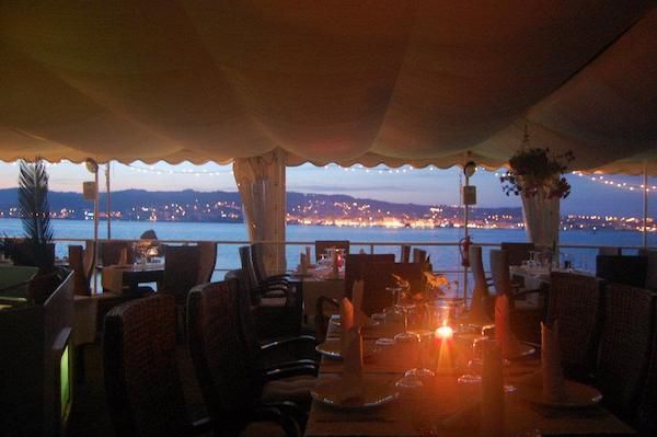 Sala apparecchiata al tramonto, con le luci della costa sullo sfondo